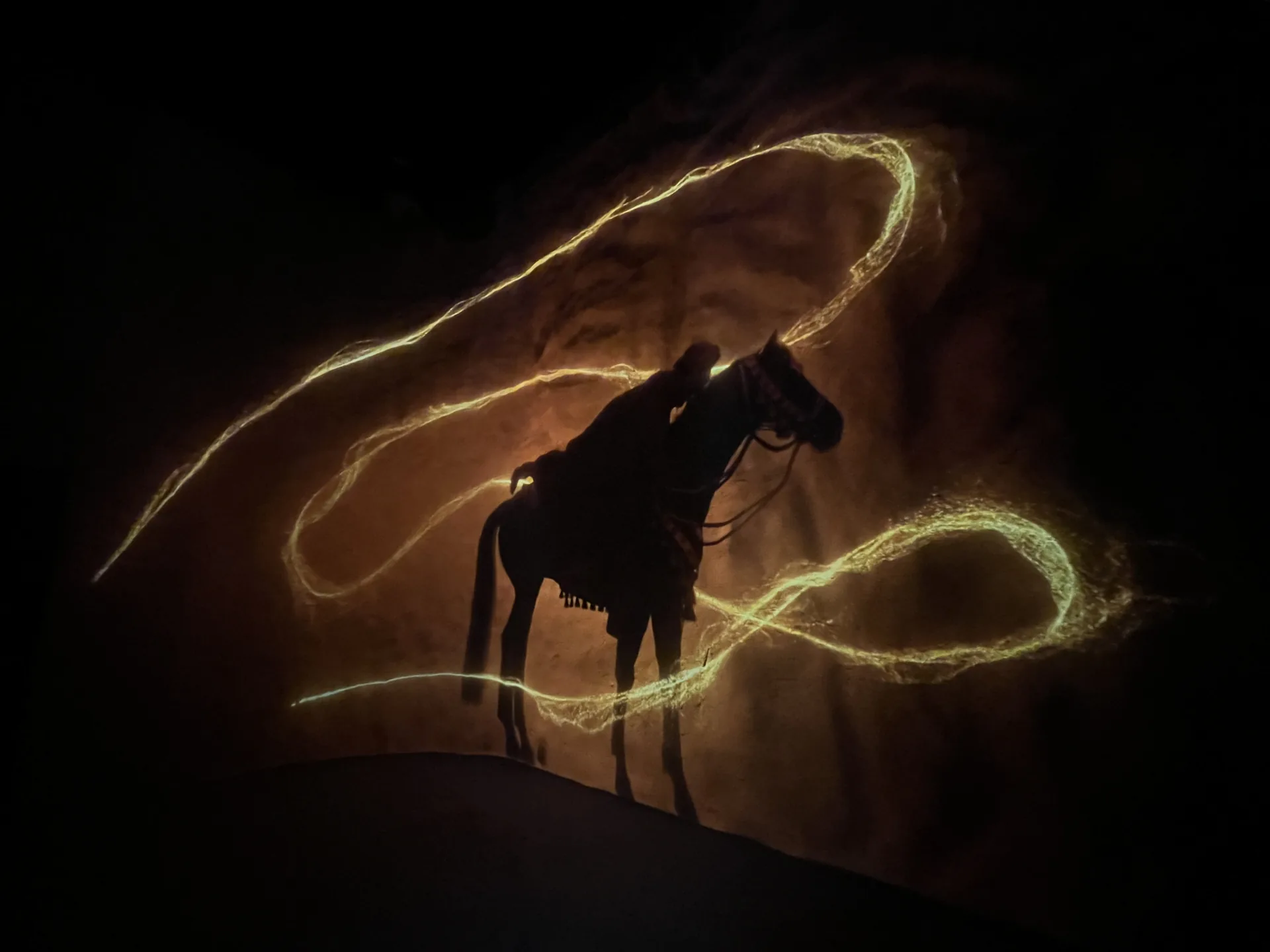 Silhouette of a rider against golden projected light trails in the Suraqah Incident Experience.